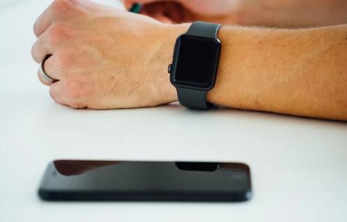 A hand wearing an Apple watch rests on a table beside an iPhone